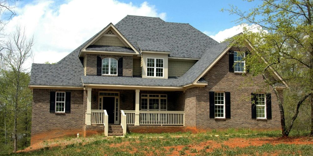 Classic two-story brick house with gable roof and front lawn in suburban setting.